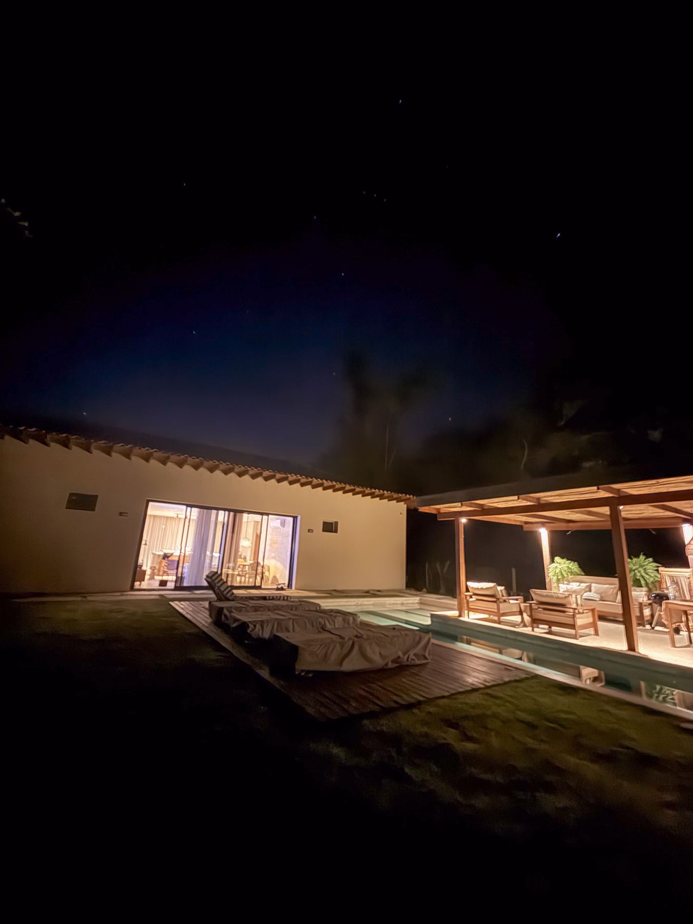 A Casa Areia à noite, com as luzes acesas, o gramado e o pergolado