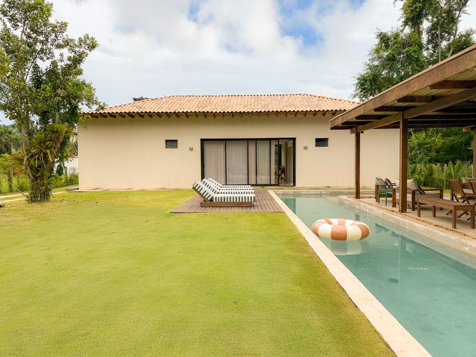 Fachada da casa de dia, com gramado e a piscina de raia